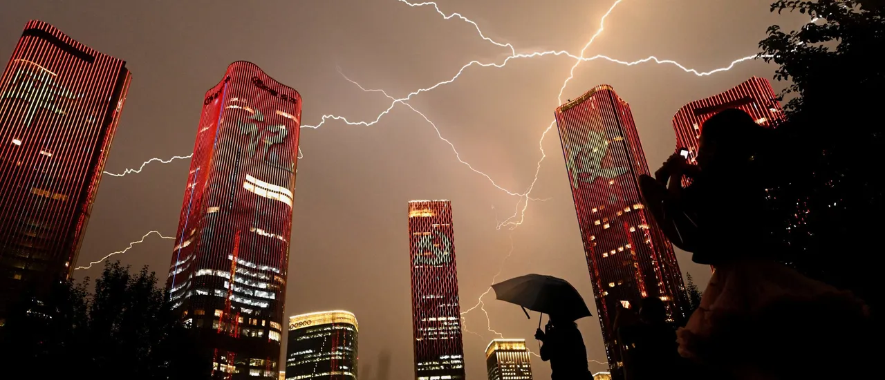 TOPSHOT - A bolt of lightning crosses the sky as people look at buildings displaying a light show on the eve of the 100th anniversary of the Chinese Communist Party in Beijing on June 30, 2021. (Photo by NOEL CELIS/AFP via Getty Images)