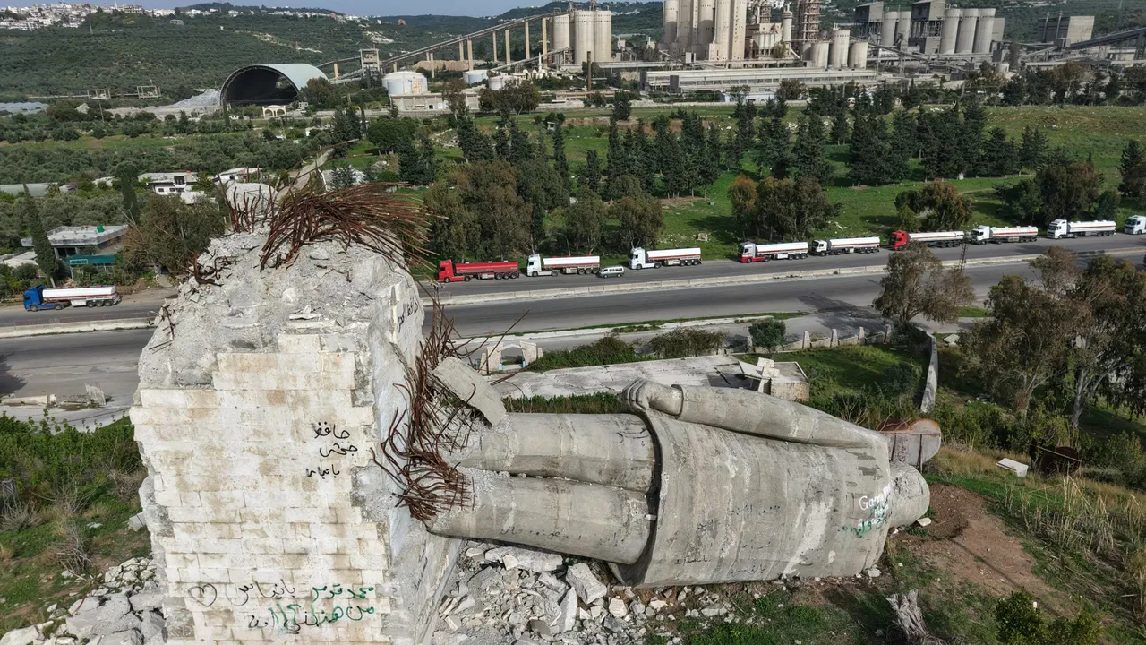 An aerial photograph shows a destroyed statue of the late Syrian president Hafez al-Assad, as a long line of Iraqi diesel-laden tanker trucks line up along the Tartus-Baniyas highway waiting to unload their cargo at the Baniyas port refinery on the Mediterranean Sea, on April 15, 2026. (Photo by Bakr ALkasem / AFP via Getty Images)