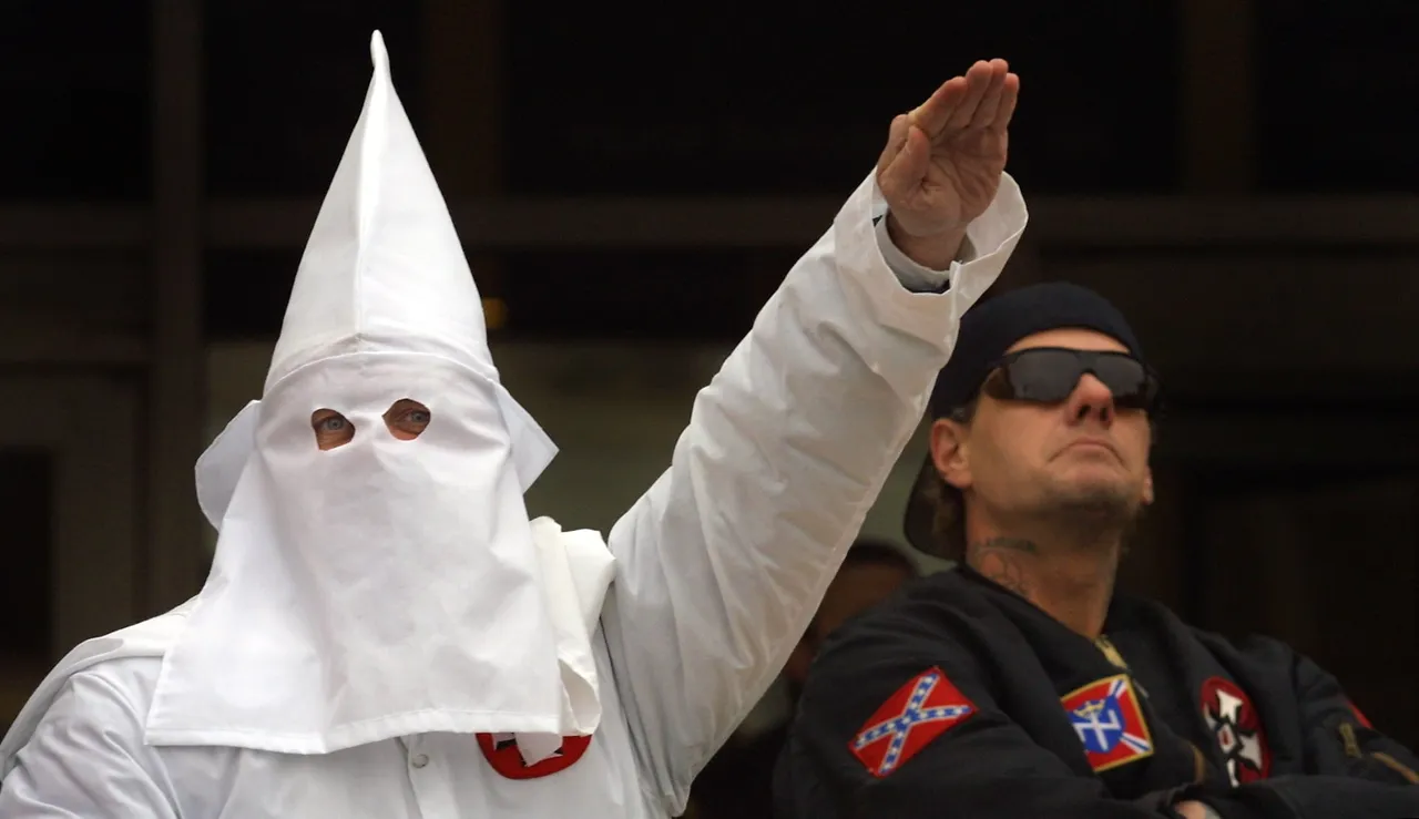 A hooded Klansman raises his left arm while another looks into the crowd during a Ku Klux Klan rally December 16, 2000 in Skokie, IL (Photo by Tim Boyle/Newsmakers)