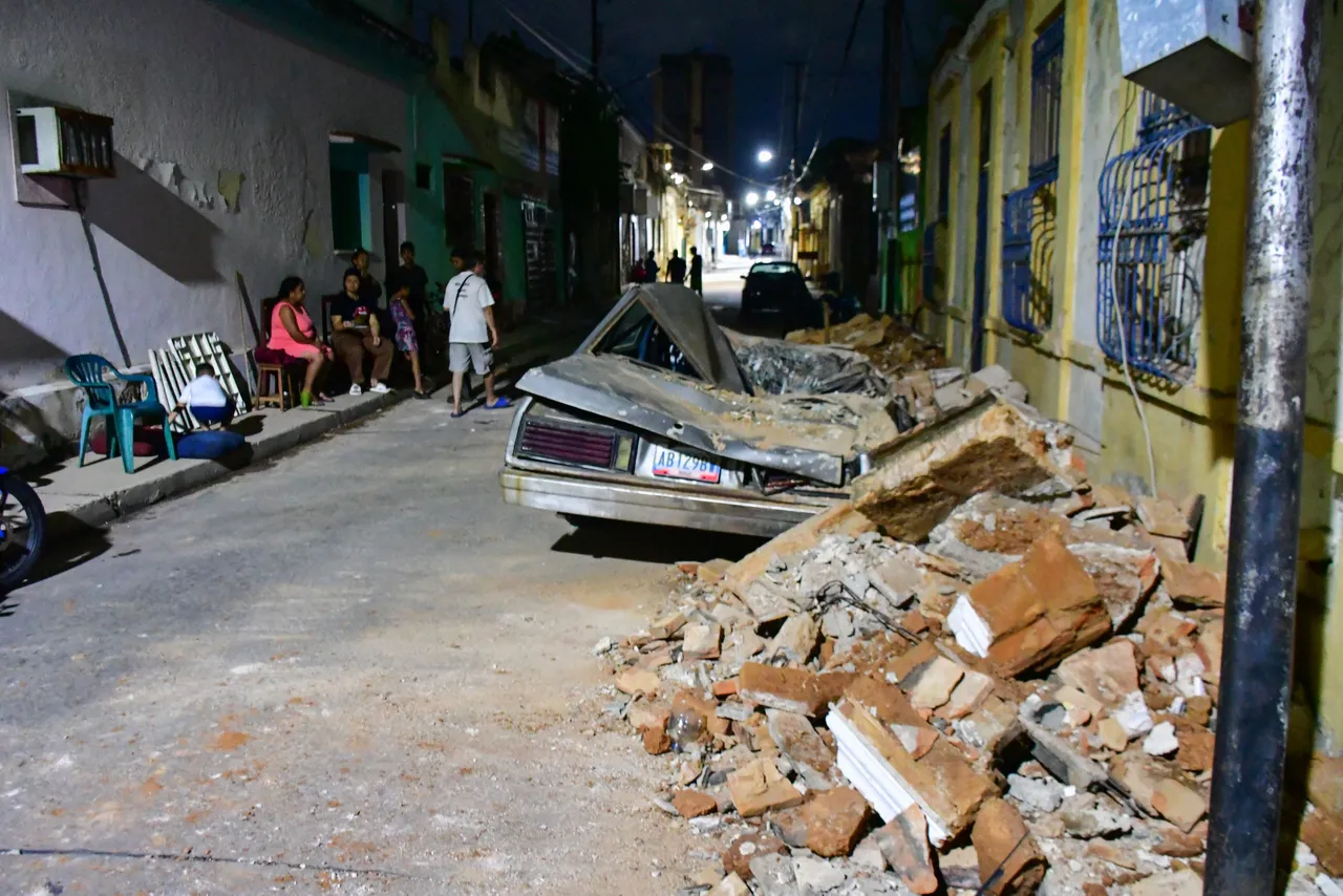 People gather on a street next to a damaged car and building following an earthquake in Valencia, Venezuela on June 24, 2026. Two earthquakes of magnitude 7.2 and 7.5 struck the same area of Venezuela on the evening of June 24, causing buildings to collapse, according to the United States Geological Survey (USGS) and AFP journalists. The quakes drove residents of the capital, Caracas, into the streets. (Photo by Jacinto OLIVEROS / AFP via Getty Images)