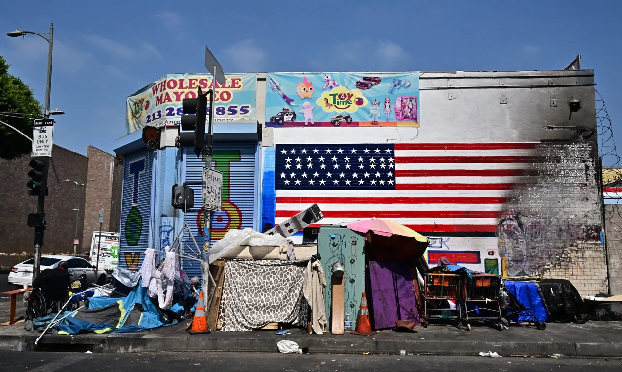 The flag of the United States is seen partially destroyed on a wall behind a homeless encampment in Los Angeles, California on August 13, 2025. (Photo by FREDERIC J. BROWN/AFP via Getty Images)
