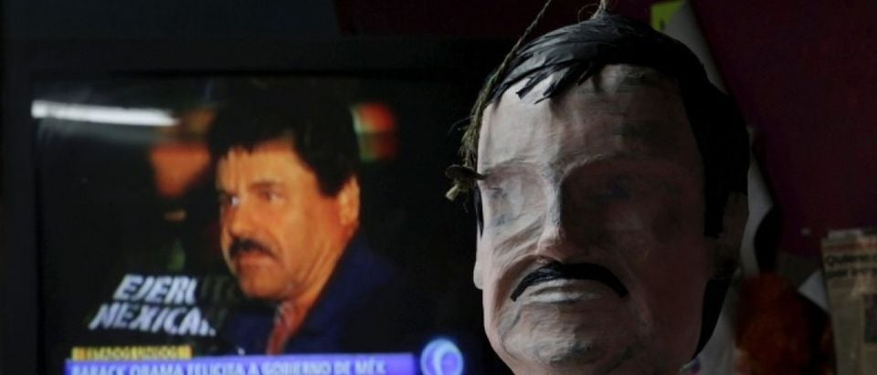 A pinata in progress depicting the drug lord Joaquin "El Chapo" Guzman is seen in front of a television showing a news bulletin of him at a workshop in Reynosa