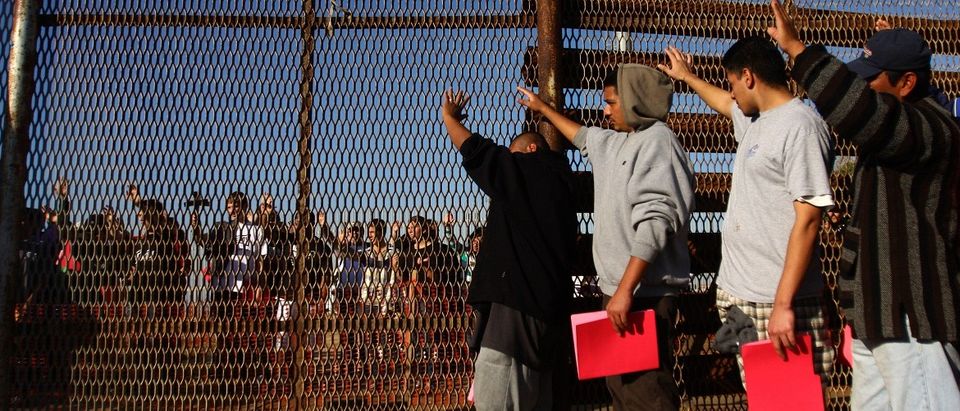 A group of recently deported immigrants stand near the double steel fence that separates San Diego and Tijuana at the border in Tijuana