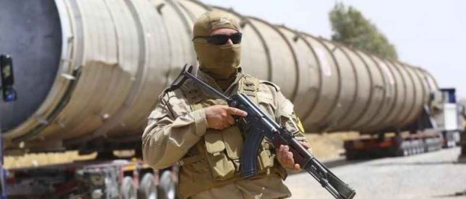 A member of the Kurdish security forces takes up position with his weapon as he guards a section of an oil refinery, which is being brought on a truck to Kalak refinery in the outskirts of Arbil