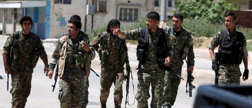 Kurdish fighters from the People's Protection Units (YPG) walk along a street in the southeast of Qamishli city