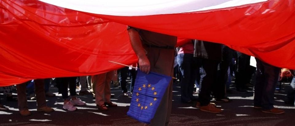 A man stands under a giant Polish flag during anti-government demonstration organized by main opposition parties in Warsaw