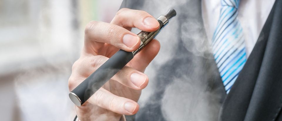Businessman holds vaporizer and is smoking electronic cigarette. (Credit: Shutterstock/vchal)