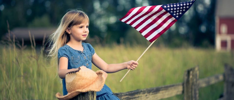 Little girl with American flag sitting on the fence