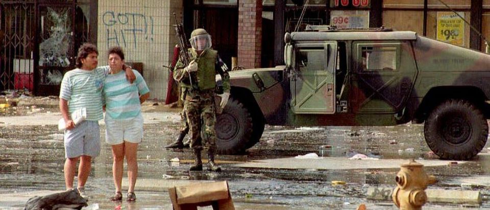 A member of the National Guard patrols the front of a Los Angeles shopping center 30 April 1992 as a couple embrace. The National Guard was brought in to control the rioting and looting. [Getty Images]