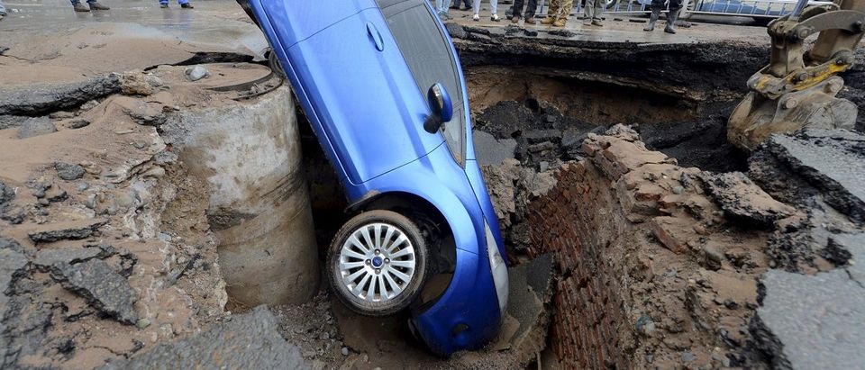 Workers look on as a car is stranded in a sinkhole on a street in Lanzhou
