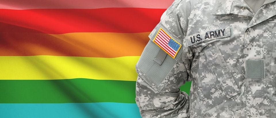 Servicemember standing in front of an LGBT flag. Niyazz/Shutterstock.