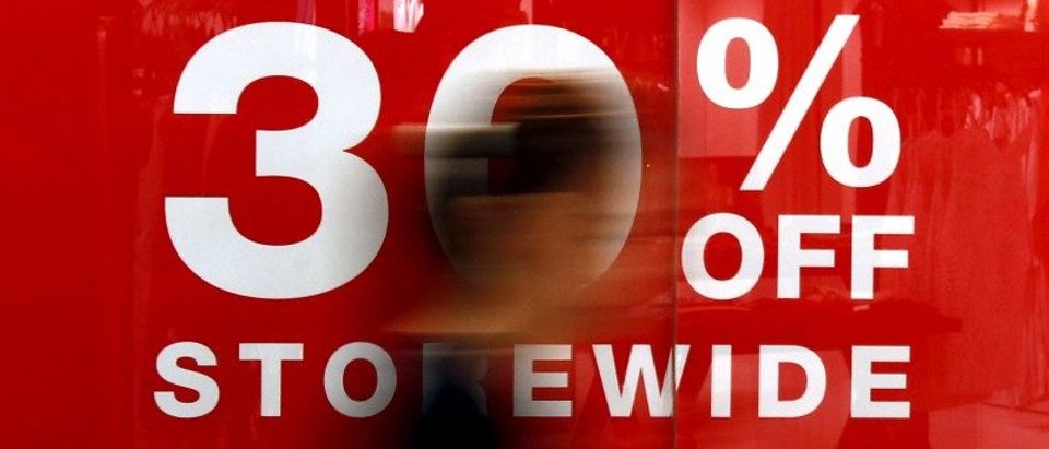 A shopper walks past a retail store displaying a sale sign in Sydney