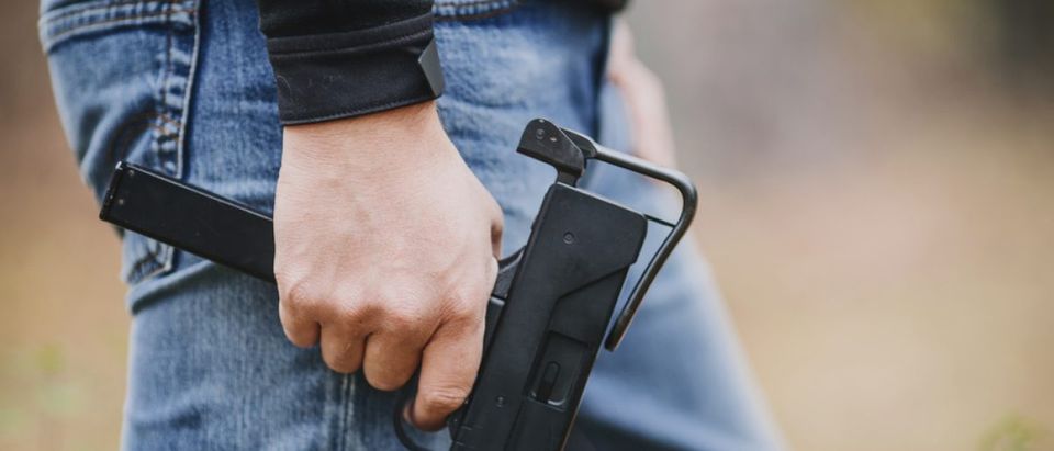 Man in jeans holding a submachine gun (Photo via Shutterstock)