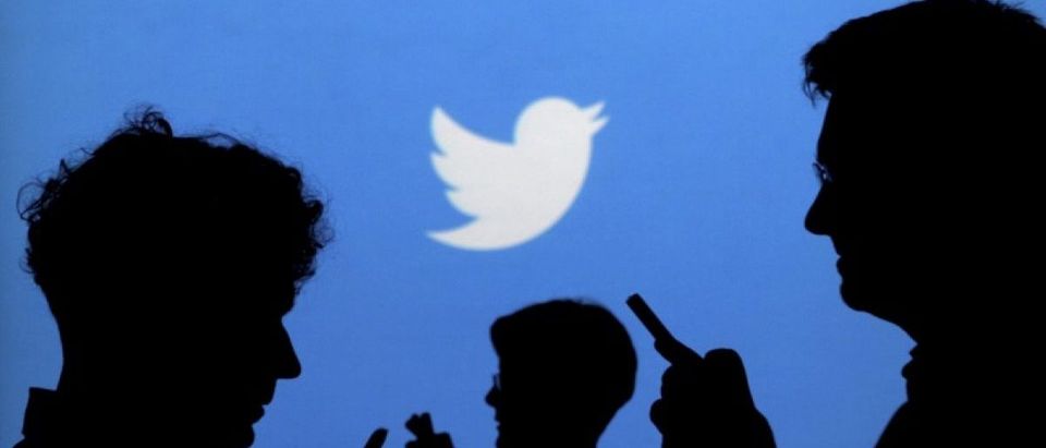 FILE PHOTO - People holding mobile phones are silhouetted against a backdrop projected with the Twitter logo
