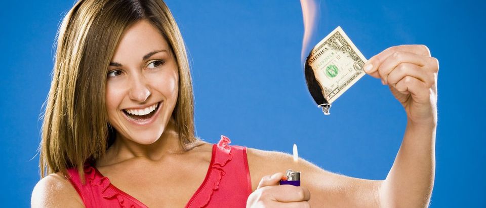 Woman setting American one dollar bill on fire (Shutterstock/Alan Bailey)