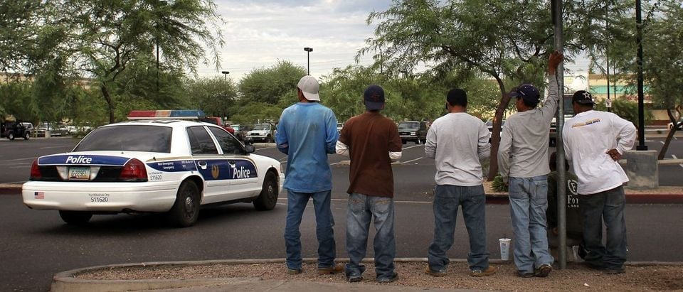 Undocumented immigrants stand on a curbside awaiting day labor work as a police patrol passes by July 26, 2010 in Phoenix, Arizona. (Photo by John Moore/Getty Images)