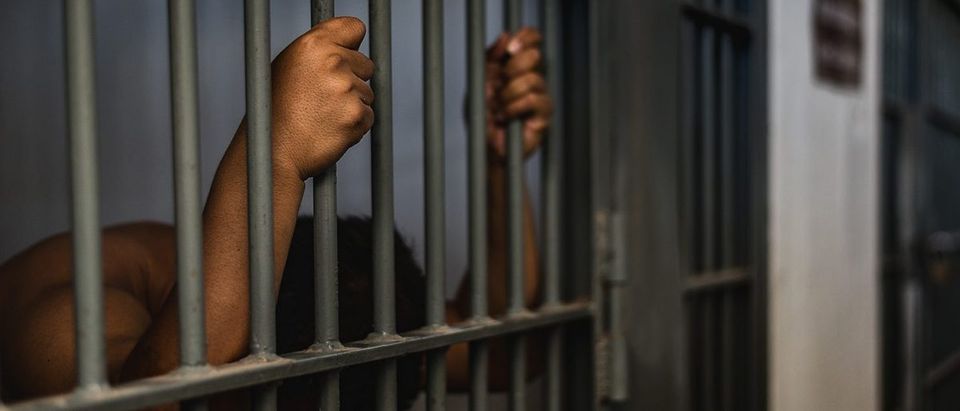 An inmate leans on jail bars. (PHOTO: areebarbar/Shutterstock)