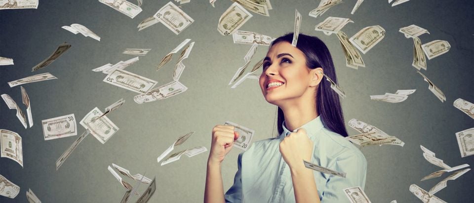 Portrait happy woman exults pumping fists ecstatic celebrates success under a money rain falling down dollar bills banknotes isolated on gray wall background with copy space (Shutterstock/pathdoc)