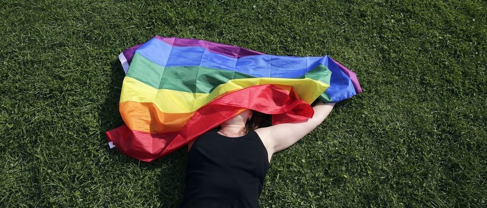 A woman with a rainbow flag lays on grass during the LGBT (lesbian, gay, bisexual, and transgender) community rally "VIII St.Petersburg Pride" in St. Petersburg