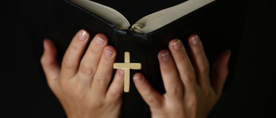 Female hands holding an open Bible with a crucifix.The concept of religion.. Credit: Studio KIWI/Shutterstock)