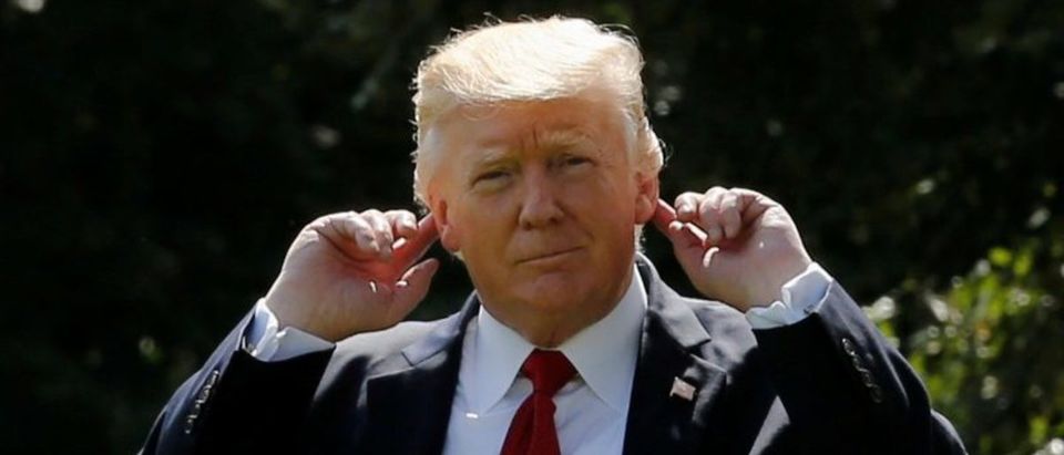 Donald Trump signals to reporters that he can't hear their questions over the helicopter engines as he departs for a weekend retreat with his cabinet at Camp David, from the White House in Washington