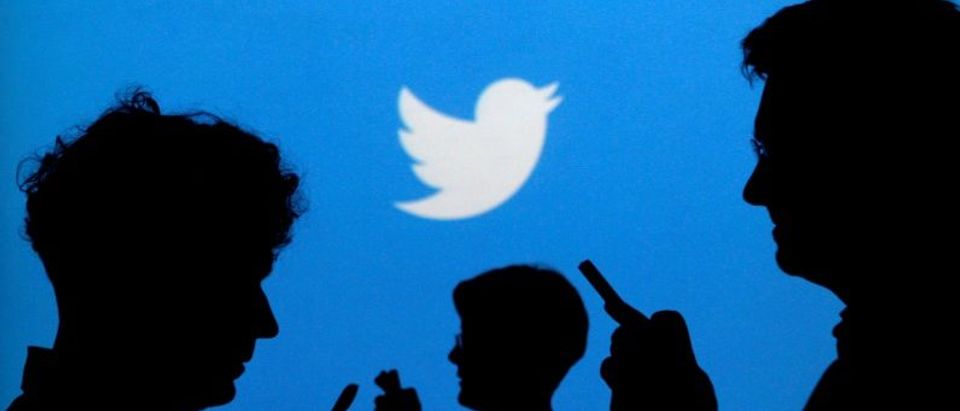 FILE PHOTO: People holding mobile phones are silhouetted against a backdrop projected with the Twitter logo
