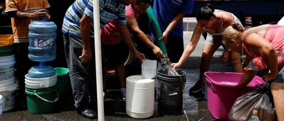 People queue to fill containers with water from a tank truck at an area hit by Hurricane Maria in Canovanas