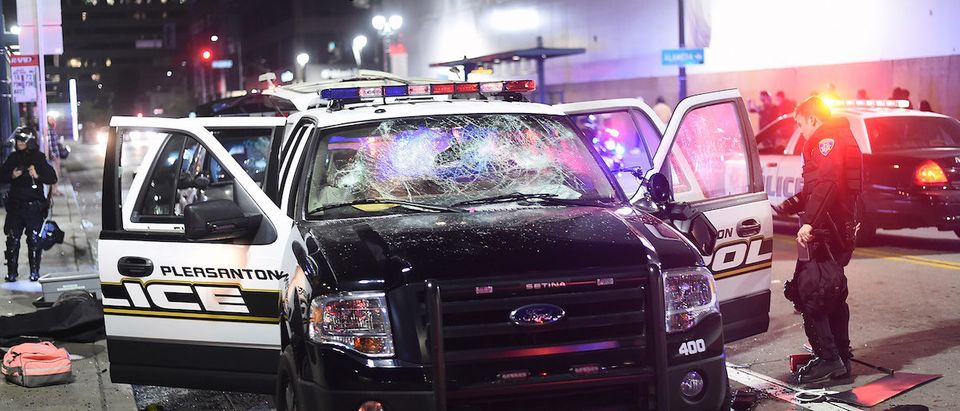 An officer examines a vandalized police vehicle as demonstrators riot in Oakland