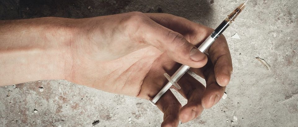 Hand addict and syringe with heroin lying on the floor. The concept of anti drugs. male drug addict hand, drugs narcotic syringe. (Fuss Sergei/Shutterstock)