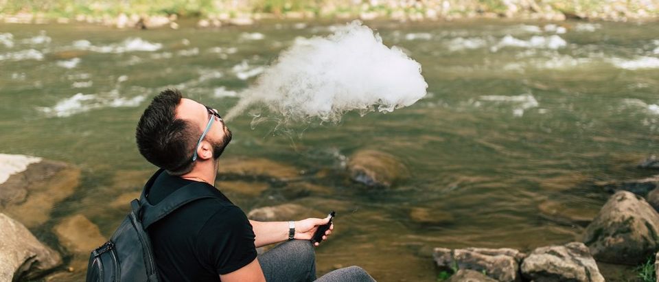 Traveler smoke electronic cigarette near mountain river. (bedya/Shutterstock)