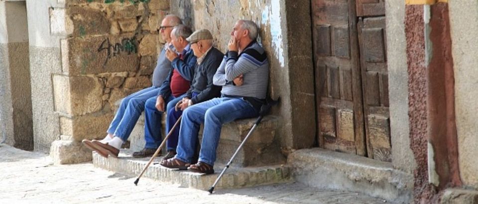 Men sitting together on stone bench, Garganta la Olla, La Vera, Extremadura, Spain. (Photo by: Geography Photos/UIG via Getty Images) | Man Legally Changes Gender To Retire