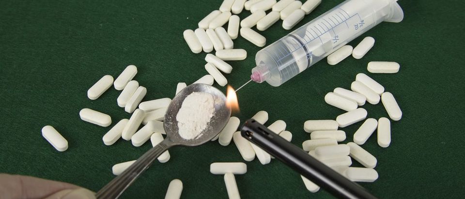 Crushed powdered opioids in spoon with lighter, pills and syringe. (karenfoleyphotography/Shutterstock)
