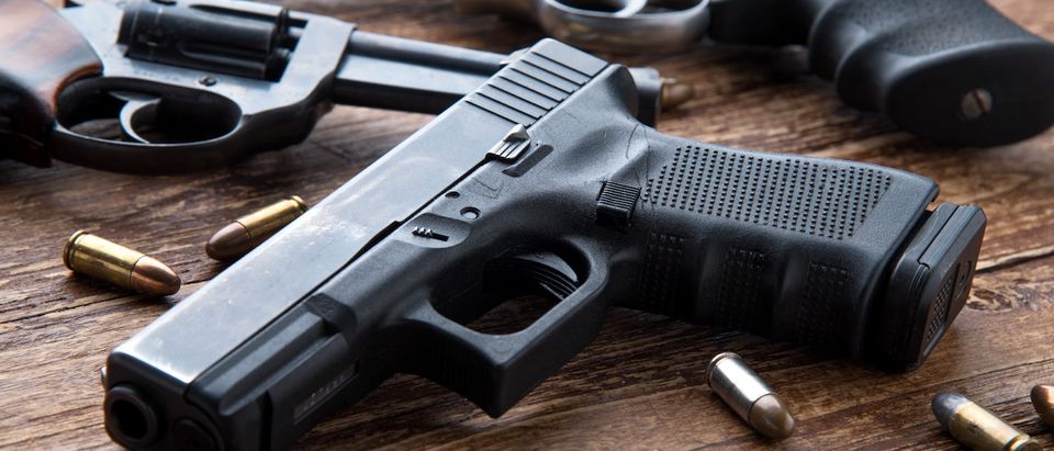Gun with ammunition on wooden background. (Shutterstock/Kiattipong)