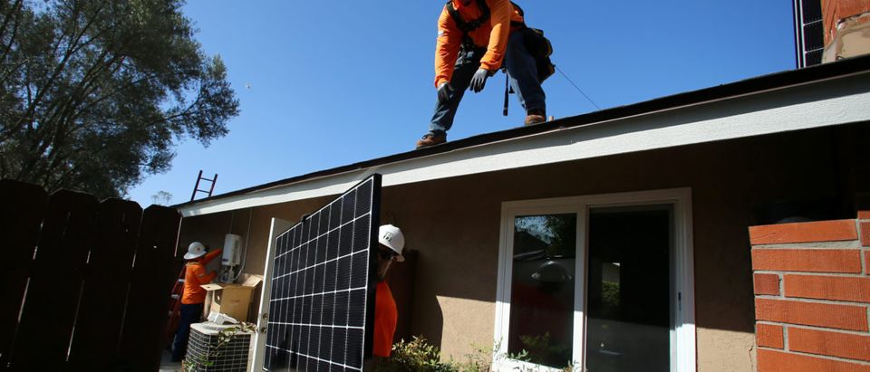 Workers lift a solar panel onto a roof during a residential solar installation in Scripps Ranch, San Diego, California