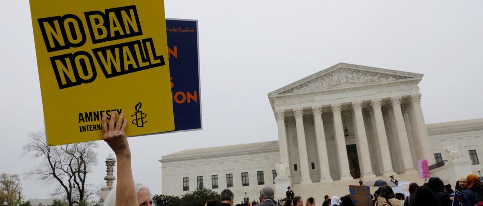 A protester holds a placard outside the U.S. Supreme Court, while the court justices consider case regarding presidential powers as it weighs the legality of President Donald Trump's latest travel ban targeting people from Muslim-majority countries, in Washington, DC, U.S., April 25, 2018. REUTERS/Yuri Gripas