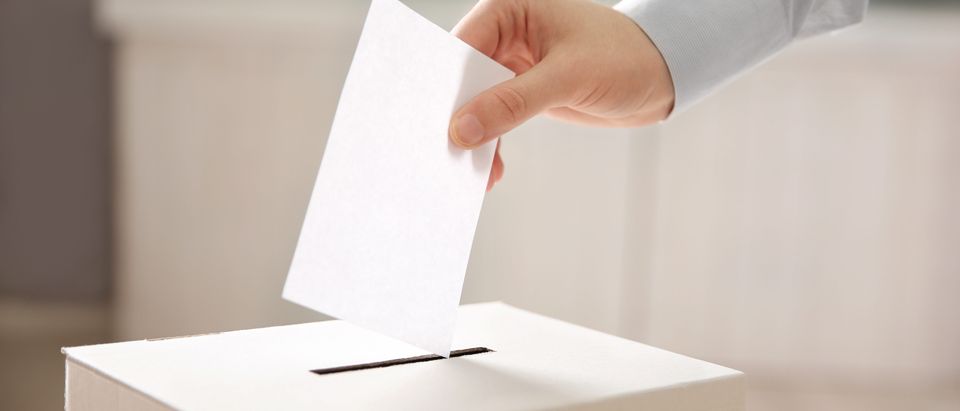 Closeup of hand inserting envelope in ballot box. (Shutterstock 570015418)