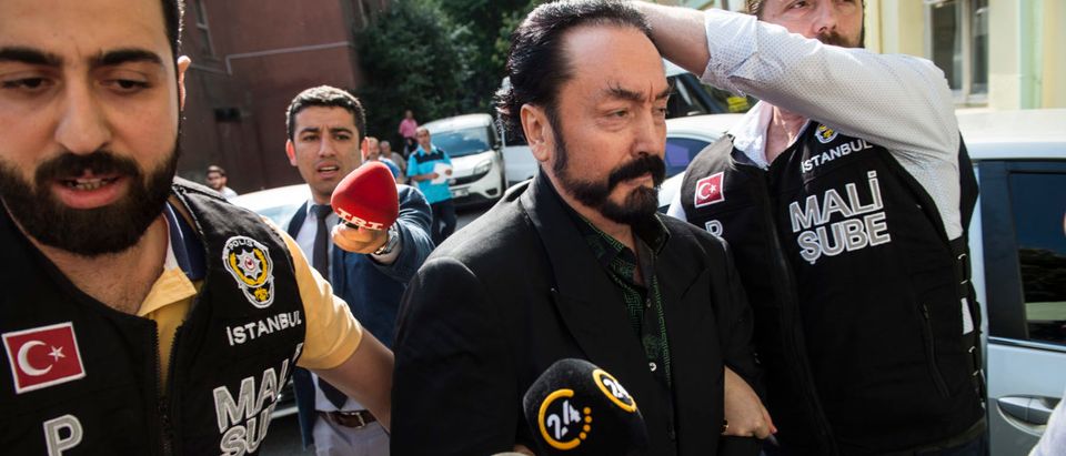 Turkish police officers escort televangelist and leader of a sect, Adnan Oktar (C) on July 11, 2018, in Istanbul, as he is arrested on fraud charges. - Turkish police detained the televangelist on fraud charges on July 11, 2018, notorious for propagating conservative views while surrounded by scantily-clad women he refers to as his "kittens." (DOGAN NEWS AGENCY/AFP/Getty Images)