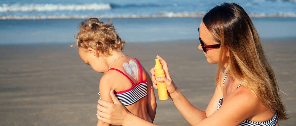Mom applies sunscreen to her child's back on the beach.