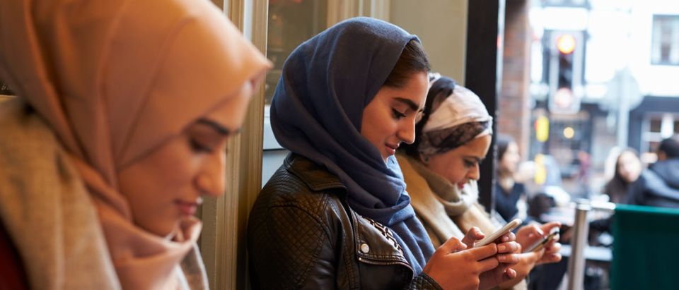 A group of Muslim women are texting outside a coffee shop. [Shutterstock/Monkey Business Images]