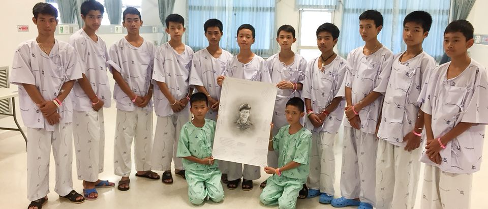 The 12-member "Wild Boars" soccer team and their coach rescued from a flooded cave pose with a drawing picture of Samarn Kunan, a former Thai navy diver who died working to rescue them at the Chiang Rai Prachanukroh Hospital, in Chiang Rai