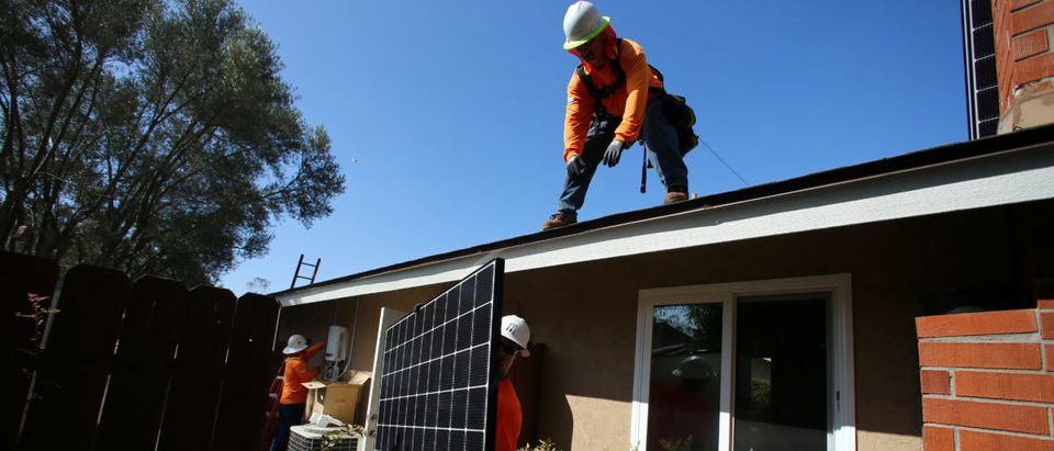 Workers lift a solar panel onto a roof during a residential solar installation in Scripps Ranch, San Diego, California