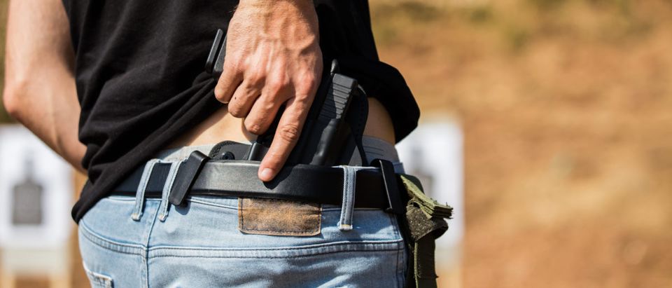 The man hid the gun behind his back. [Shutterstock/Hajrudin Hodzic]