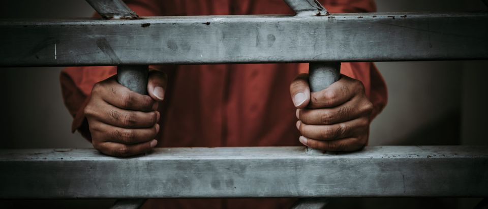 A man stands behind bars. Shutterstock image via user kittirat roekburi
