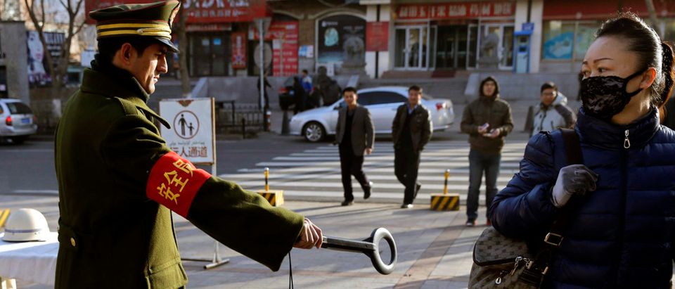 A pedestrian reacts as a security officer holds out a detector on a street in Urumqi