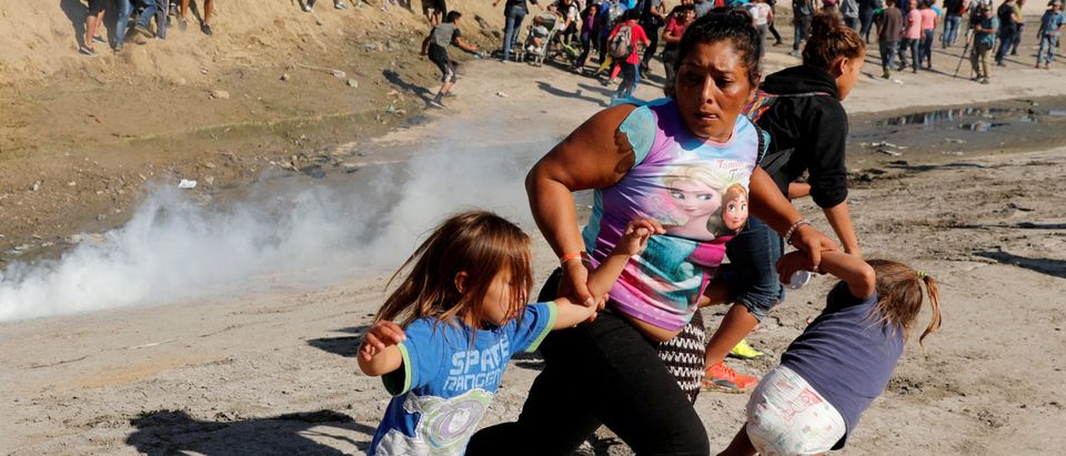 A migrant family runs away from tear gas in front of the border wall between the U.S and Mexico, in Tijuana