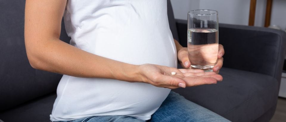 A pregnant woman holds a pill. (Shutterstock/Andrey Popov)