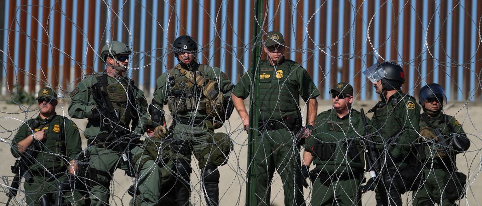 U.S border patrol stand near the border fence between Mexico and the United States as migrants stand near by in Tijuana