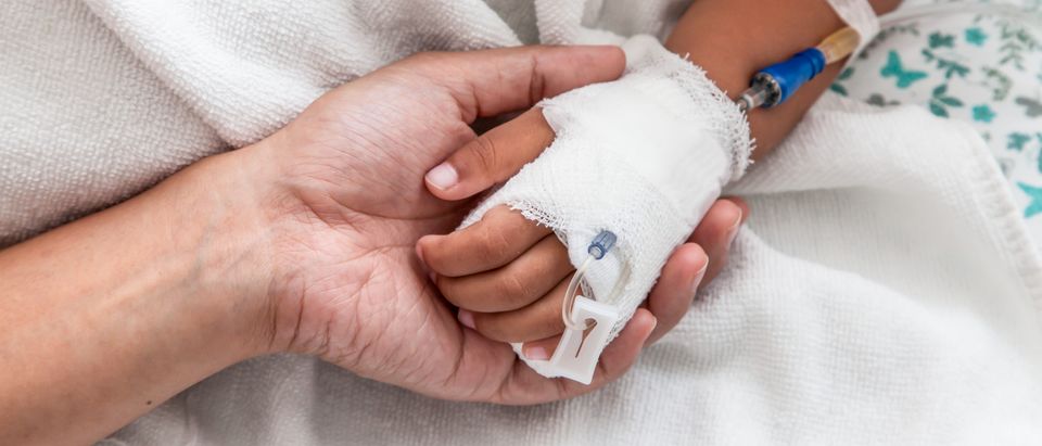 Mother holding child's hand who have IV solution in the hospital - Shutterstock.com