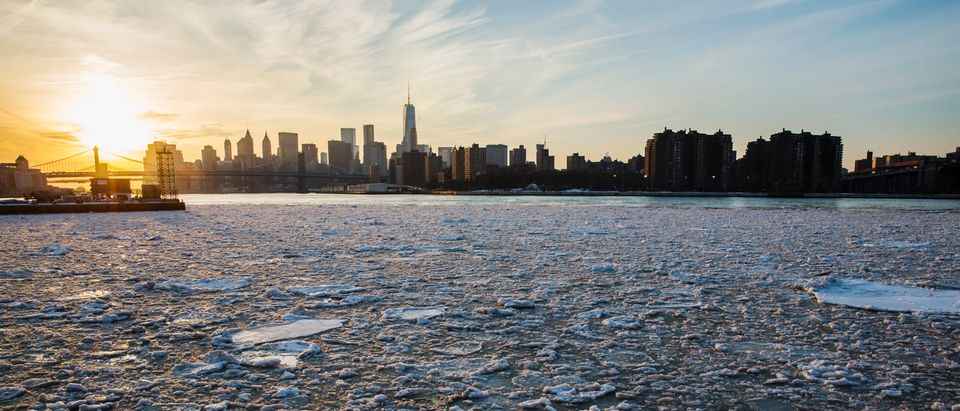 The sun sets behind the Manhattan skyline as ice floats down the East River in New York