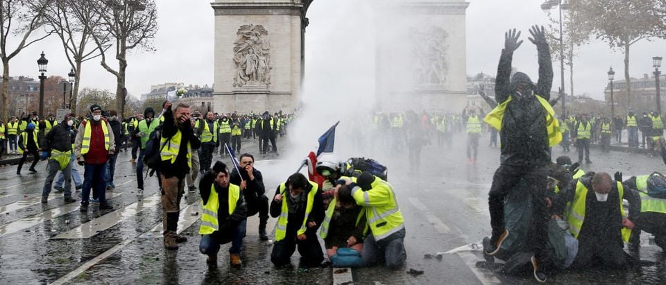 Protesters wearing yellow vests, a symbol of a French drivers' protest against higher diesel taxes, stand up in front of a police water canon at the Place de l'Etoile near the Arc de Triomphe in Paris, France, December 1, 2018. REUTERS/Stephane Mahe